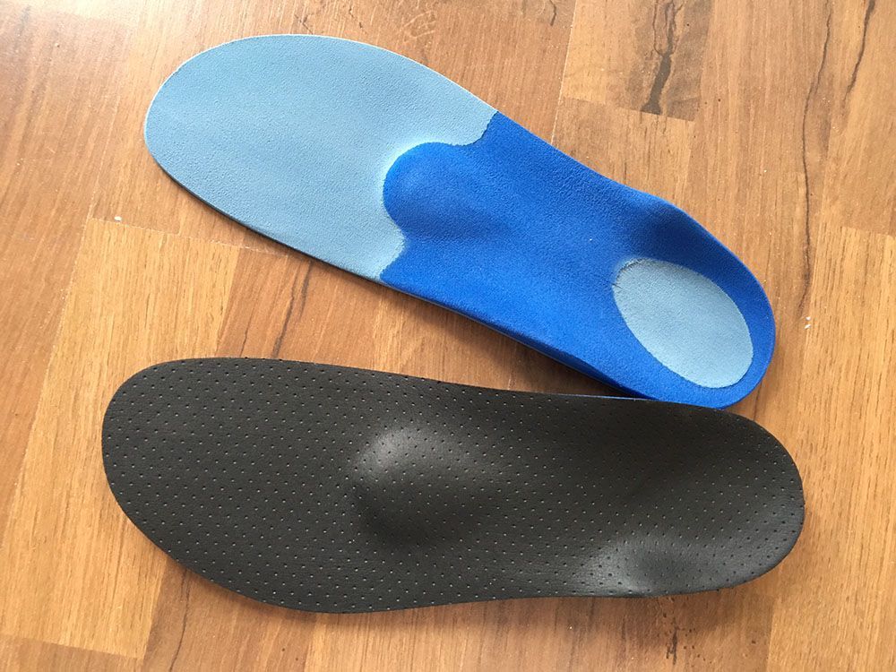 Ein Paar blaue und schwarze Einlegesohlen auf einem Holzboden