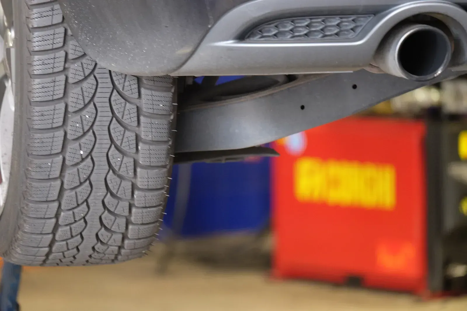Un primer pla d'un pneumàtic i un tub d'escapament d'un cotxe en un garatge.