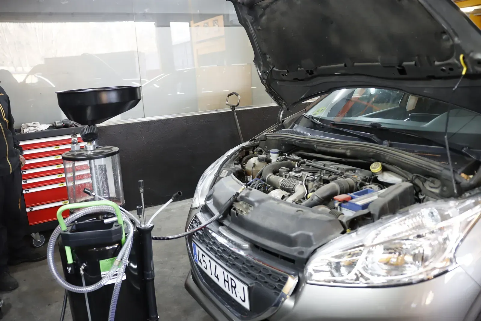S'està reparant un cotxe amb el capó obert en un garatge.