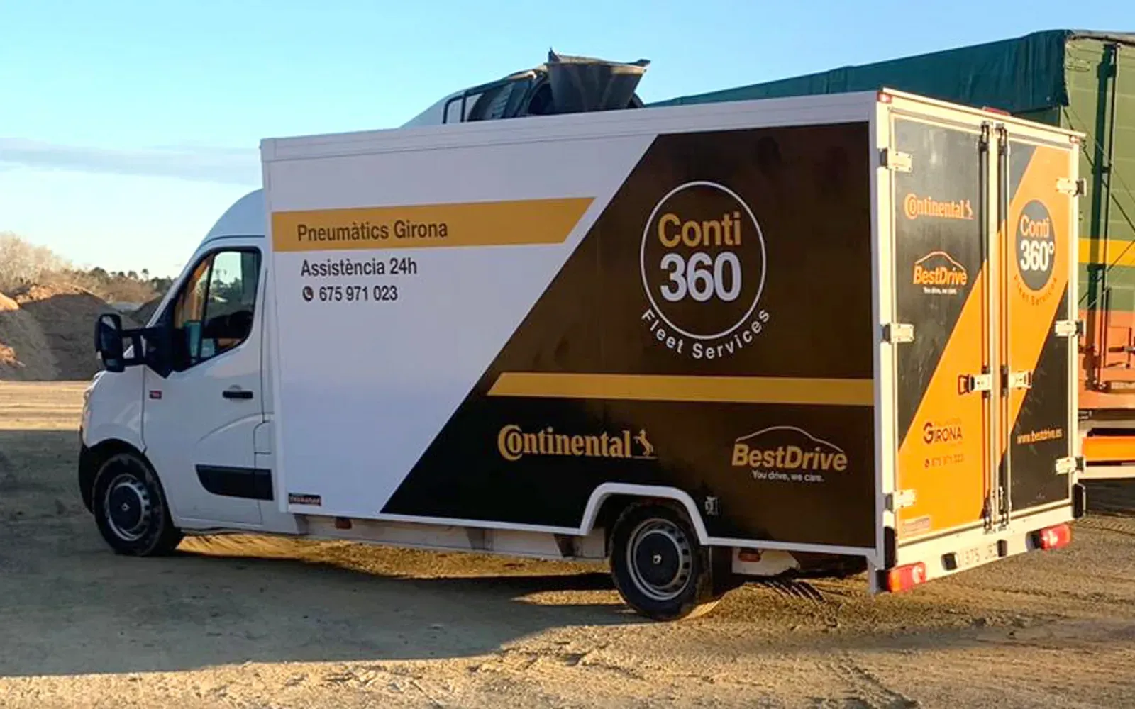 Una furgoneta blanca i marró està aparcada en un camp de terra.