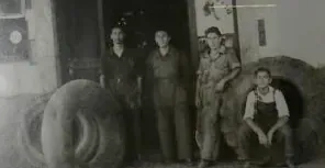 Un grup d'homes posen per a una foto davant d'un pneumàtic gran.