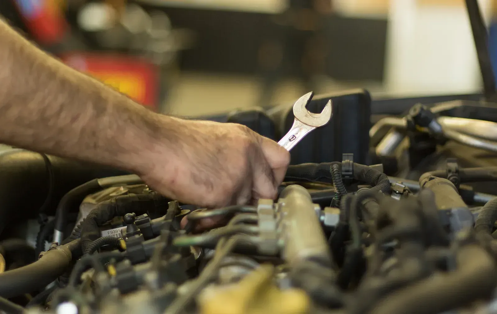 Un home està treballant en un motor de cotxe amb una clau anglesa.