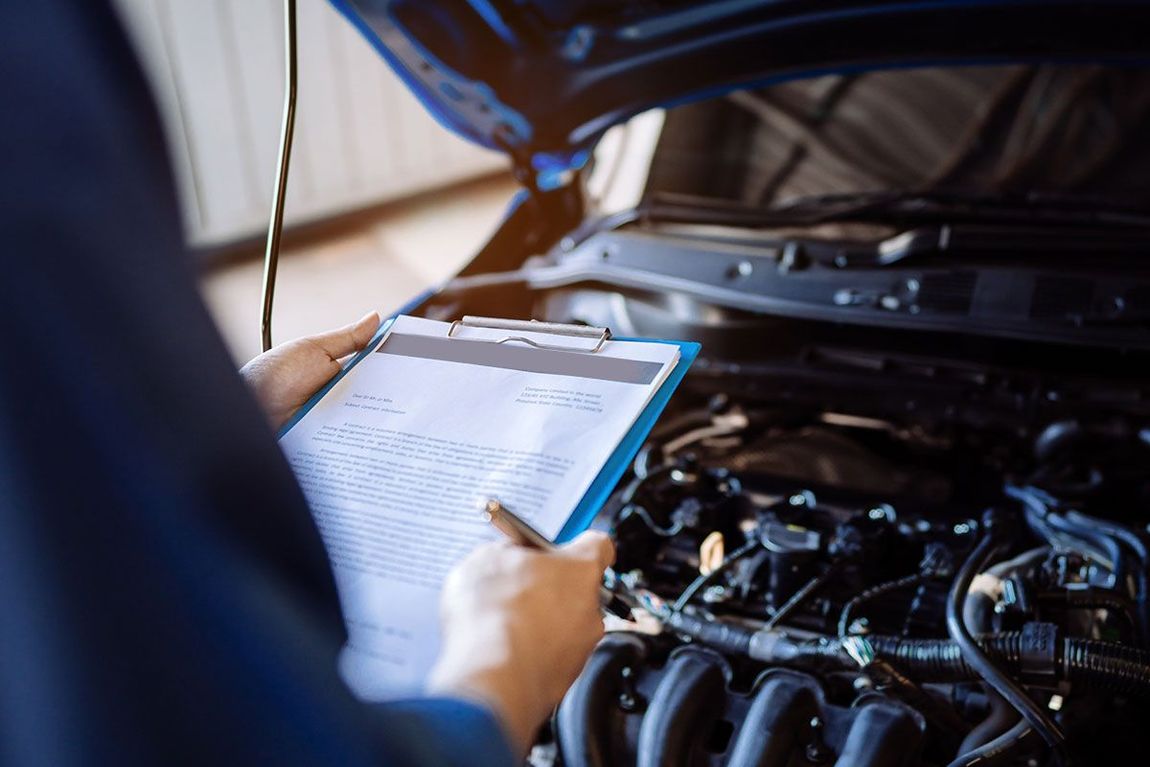 Un mecánico está escribiendo en un portapapeles mientras mira debajo del capó de un automóvil.