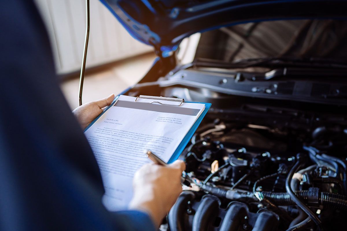 Un mecánico está escribiendo en un portapapeles mientras mira debajo del capó de un automóvil.