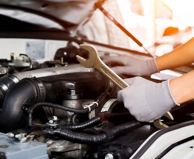 Una persona está trabajando en el motor de un automóvil con una llave inglesa.