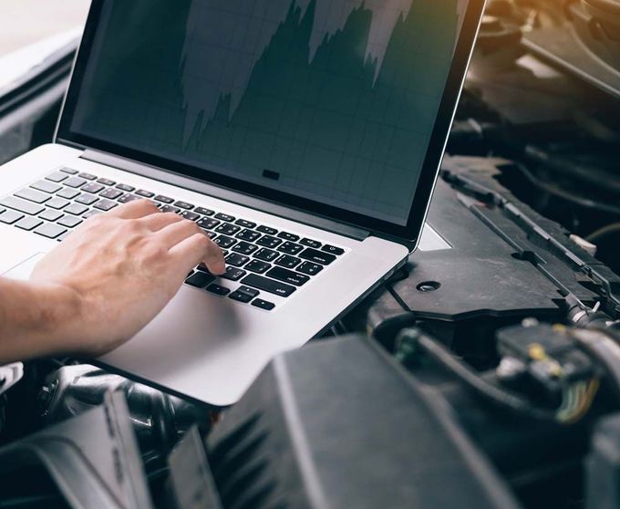 Una persona está escribiendo en una computadora portátil frente al motor de un automóvil.