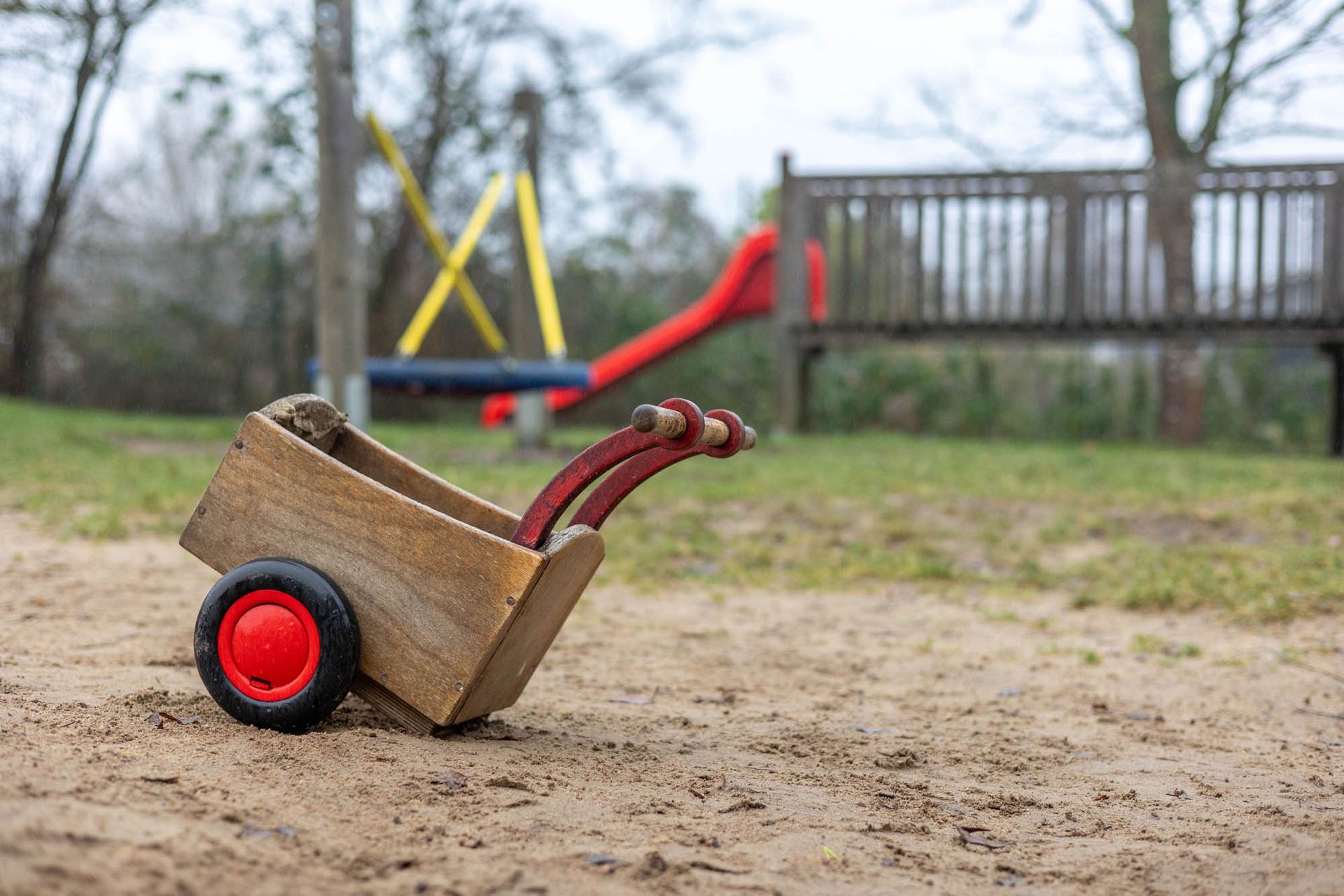 Auf einem Spielplatz steht eine hölzerne Schubkarre im Sand.