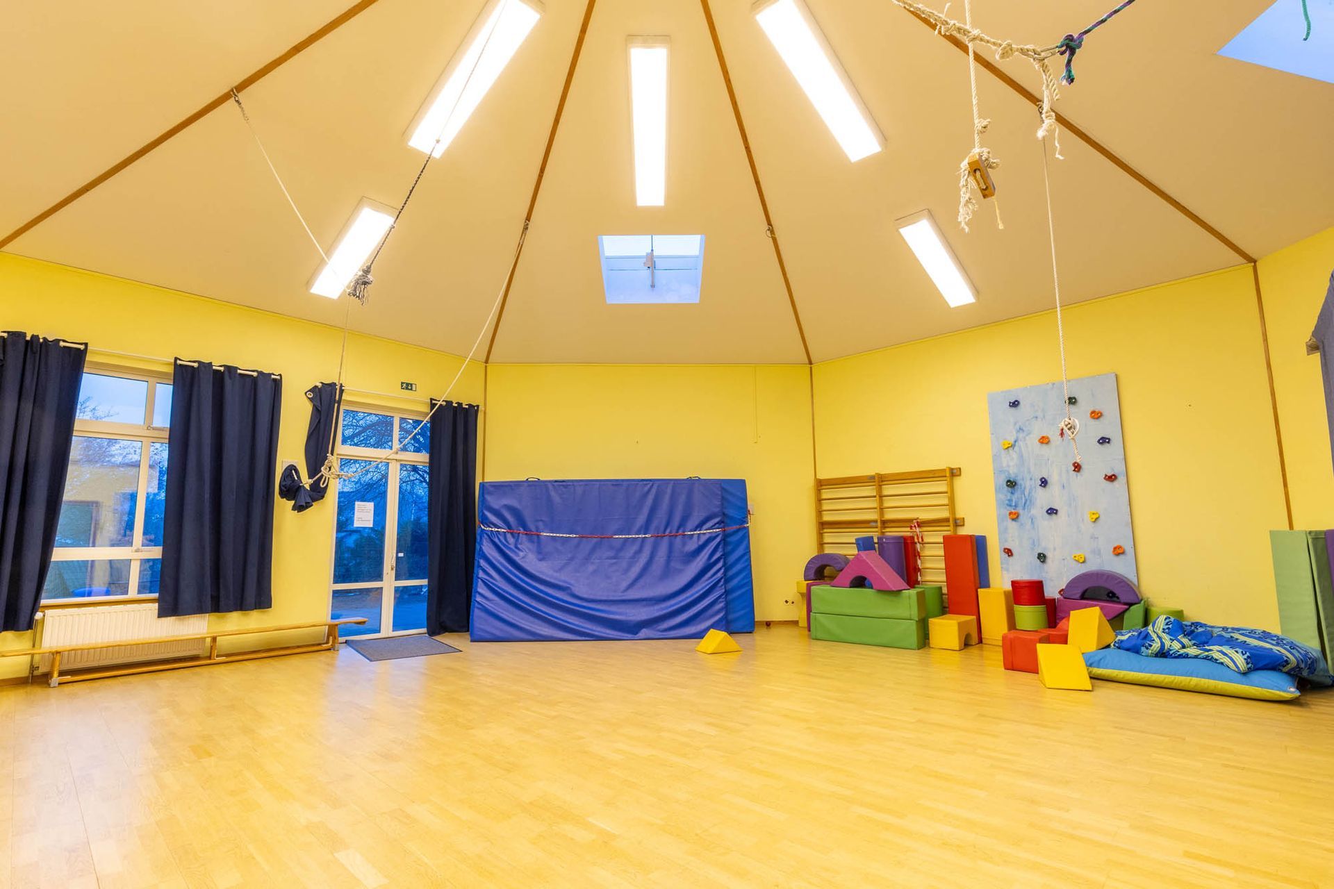 Eine große leere Turnhalle mit einer Kletterwand und vielen Spielsachen.