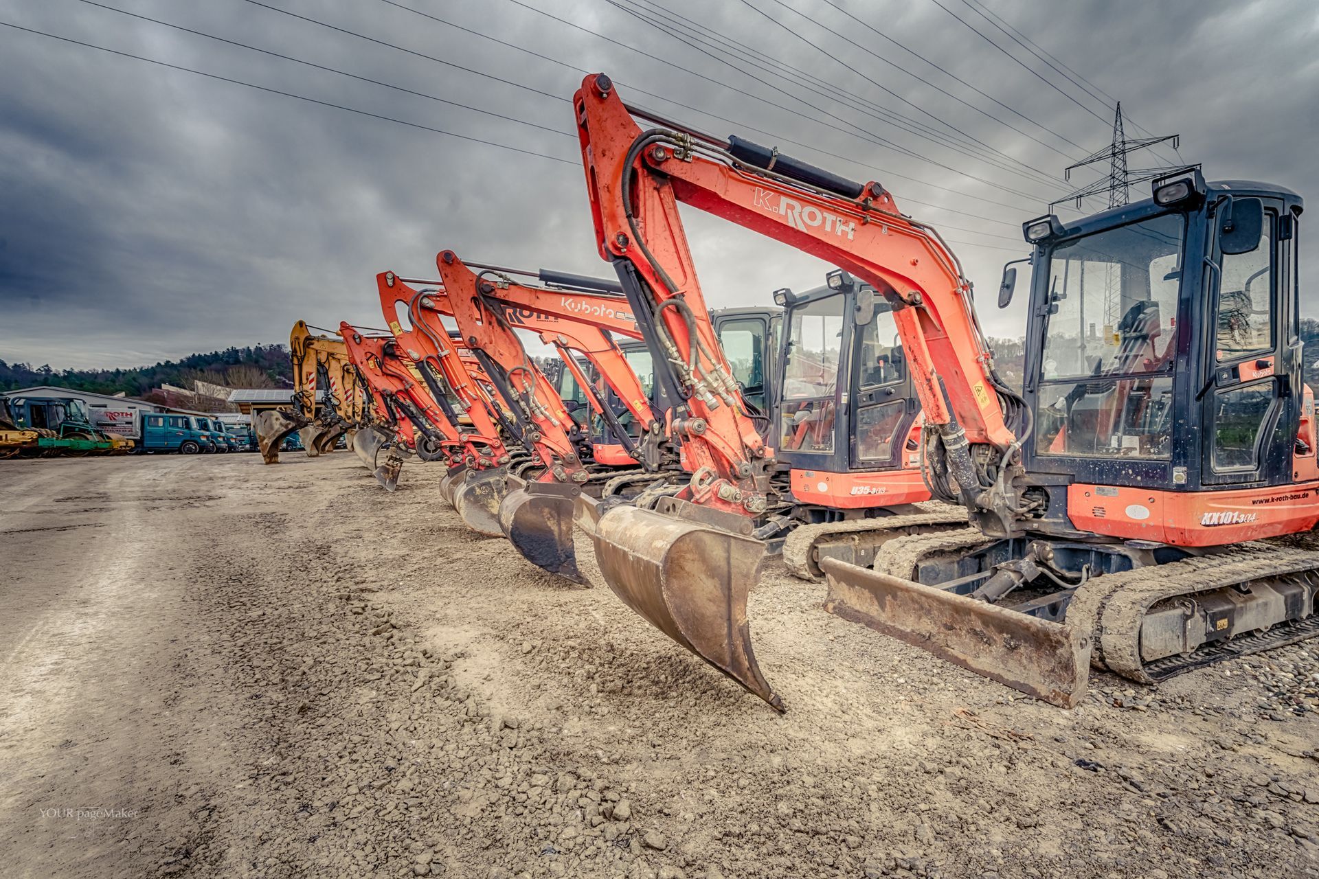 Eine Reihe von Baufahrzeugen ist auf einem unbefestigten Parkplatz geparkt.