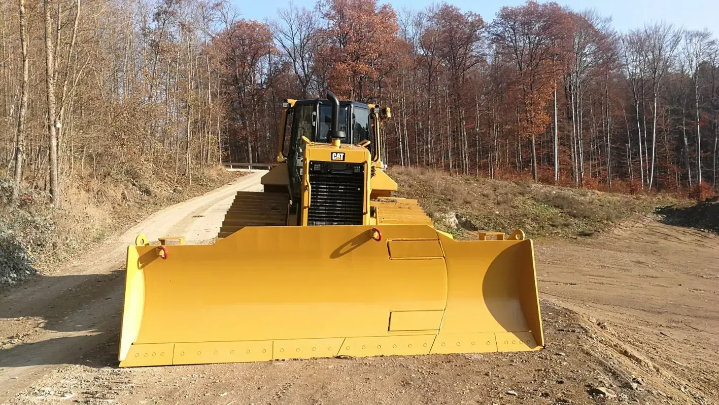 Eine Planierraupe fährt auf einem Feldweg im Wald entlang.