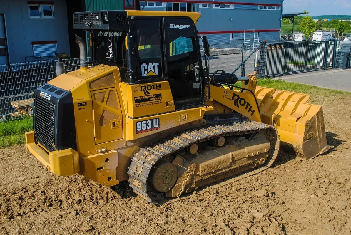 Eine gelbe Planierraupe steht im Dreck vor einem Gebäude.