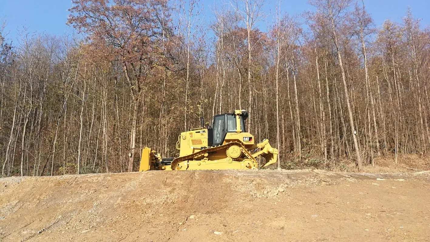 Eine Planierraupe fährt auf einer unbefestigten Straße mitten in einem Wald.