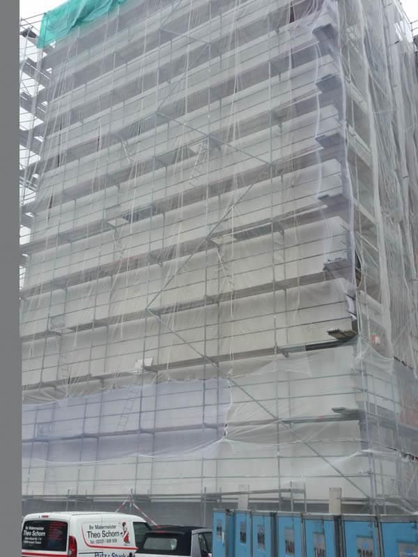 Ein großes Gebäude ist mit einem Gerüst bedeckt und davor parkt ein Bus.