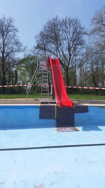 In der Mitte eines Schwimmbeckens befindet sich eine rote Rutsche.