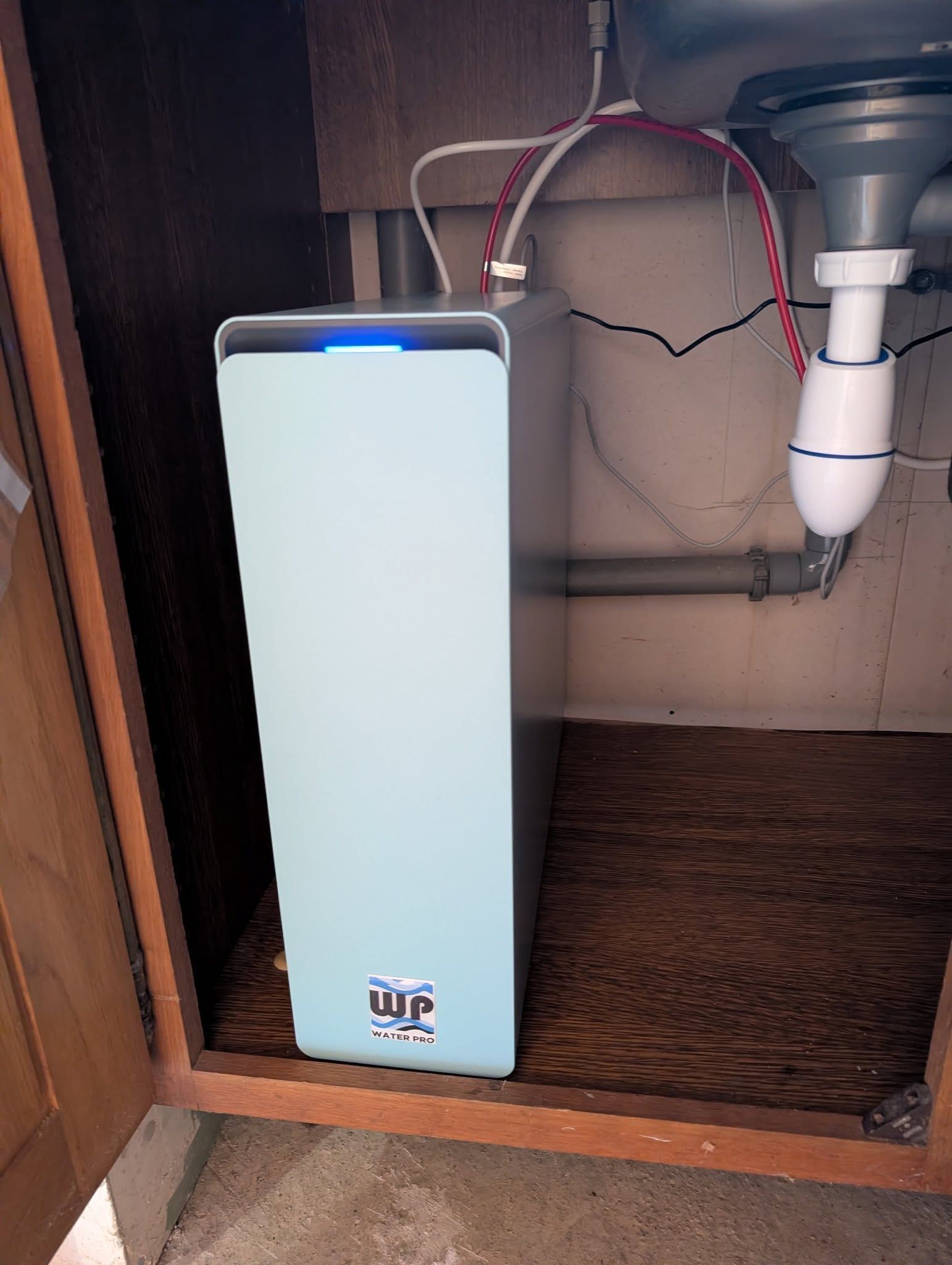 Un système de filtration d'eau bleu est installé sous l'évier, avec des tuyaux blanc et rouge.