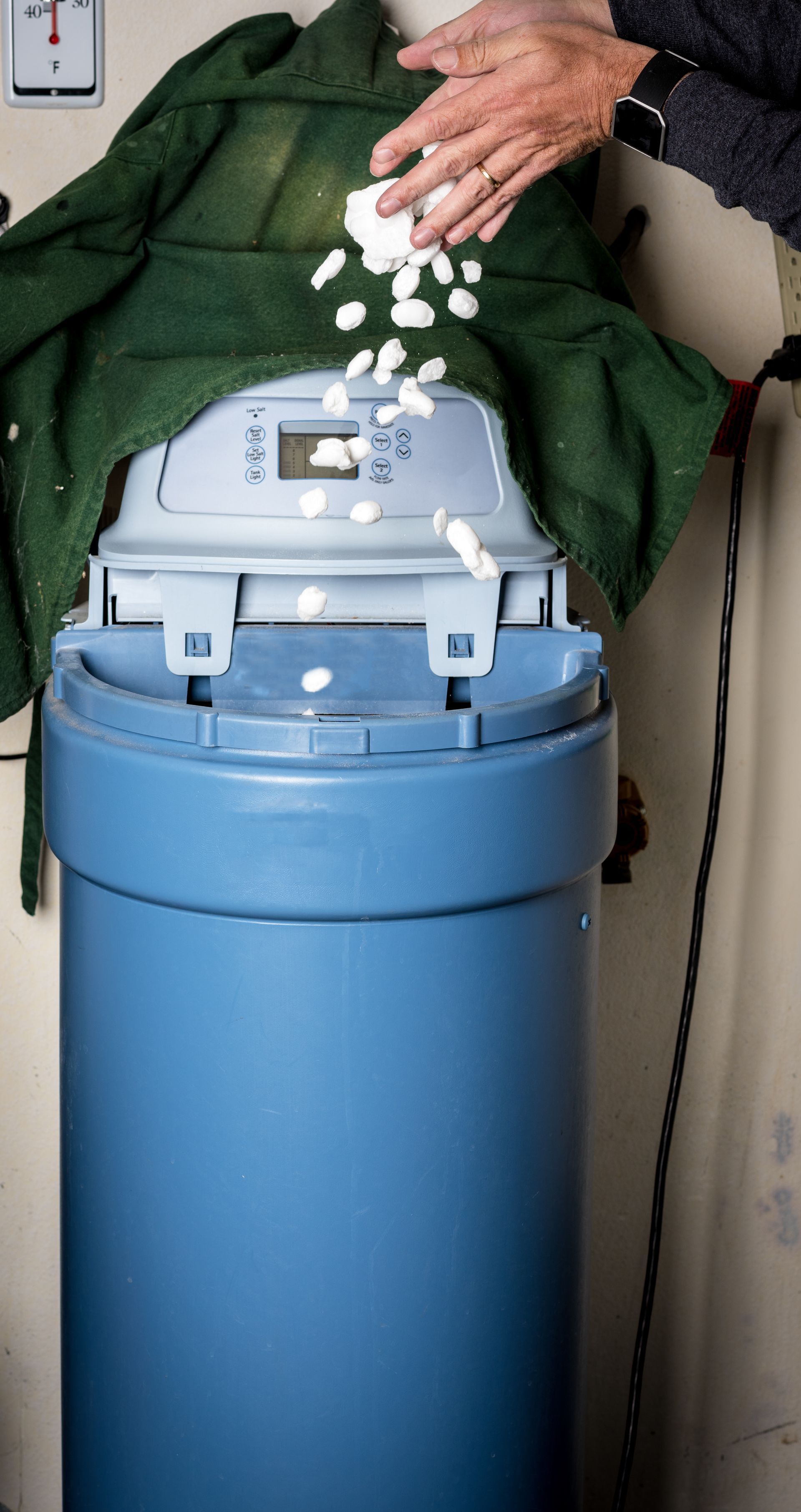 Une personne ajoute des granules de sel blanc dans un adoucisseur d'eau.