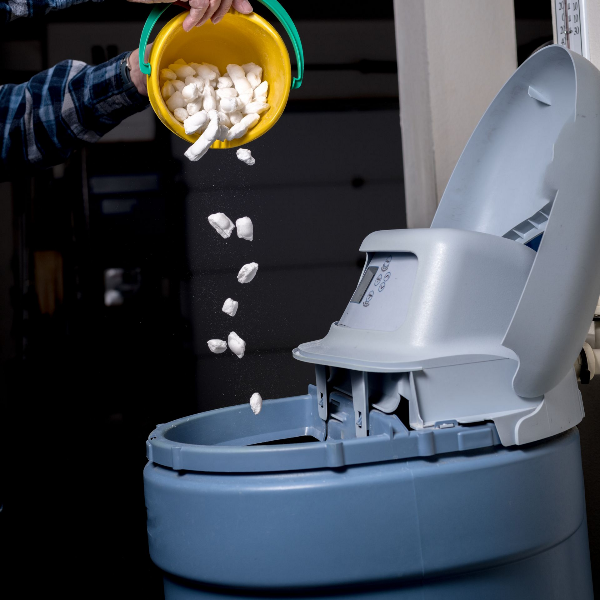 Une personne remplit un adoucisseur d'eau avec des pastilles de sel provenant d'un seau jaune.