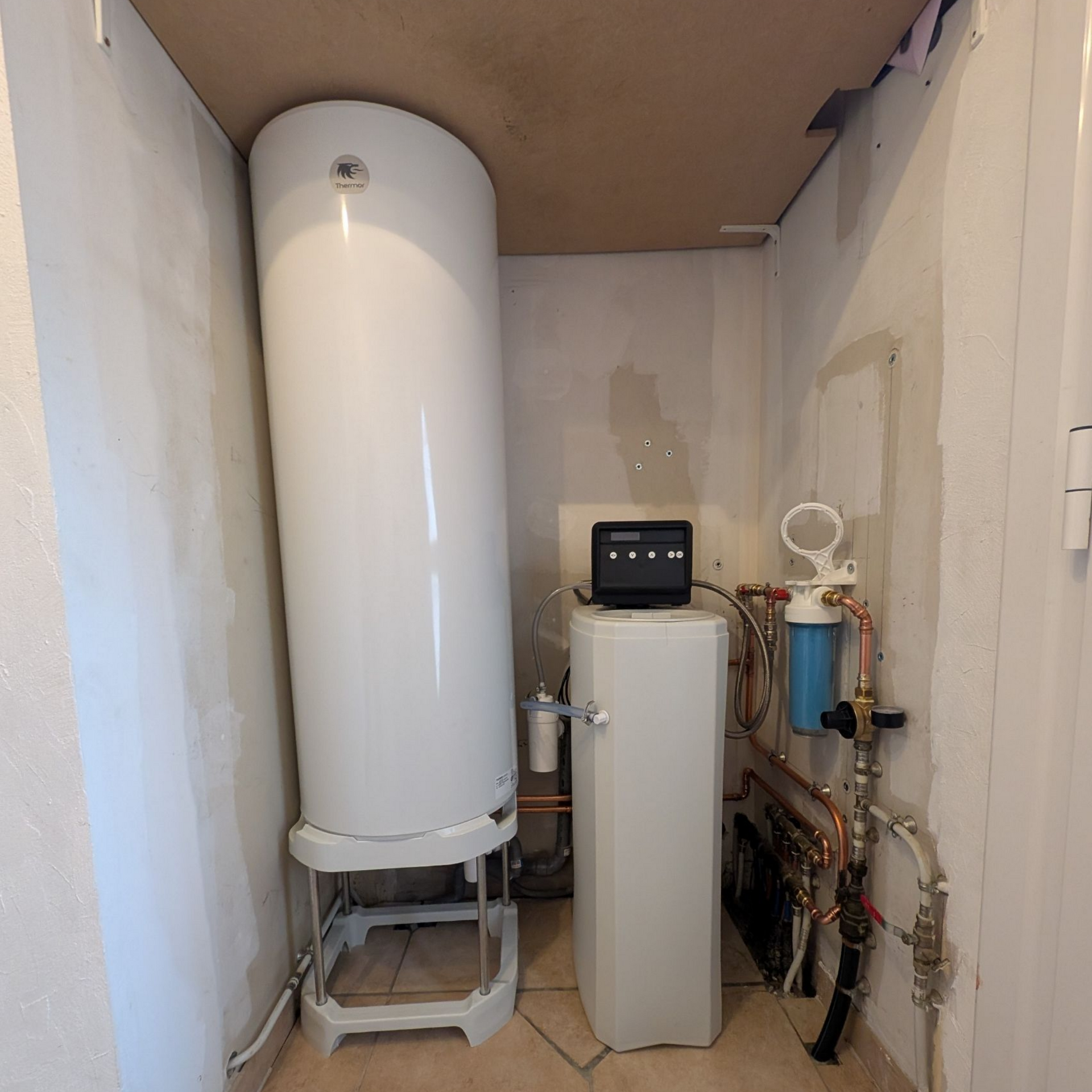 Chauffe-eau blanc et autres équipements de plomberie dans une buanderie.