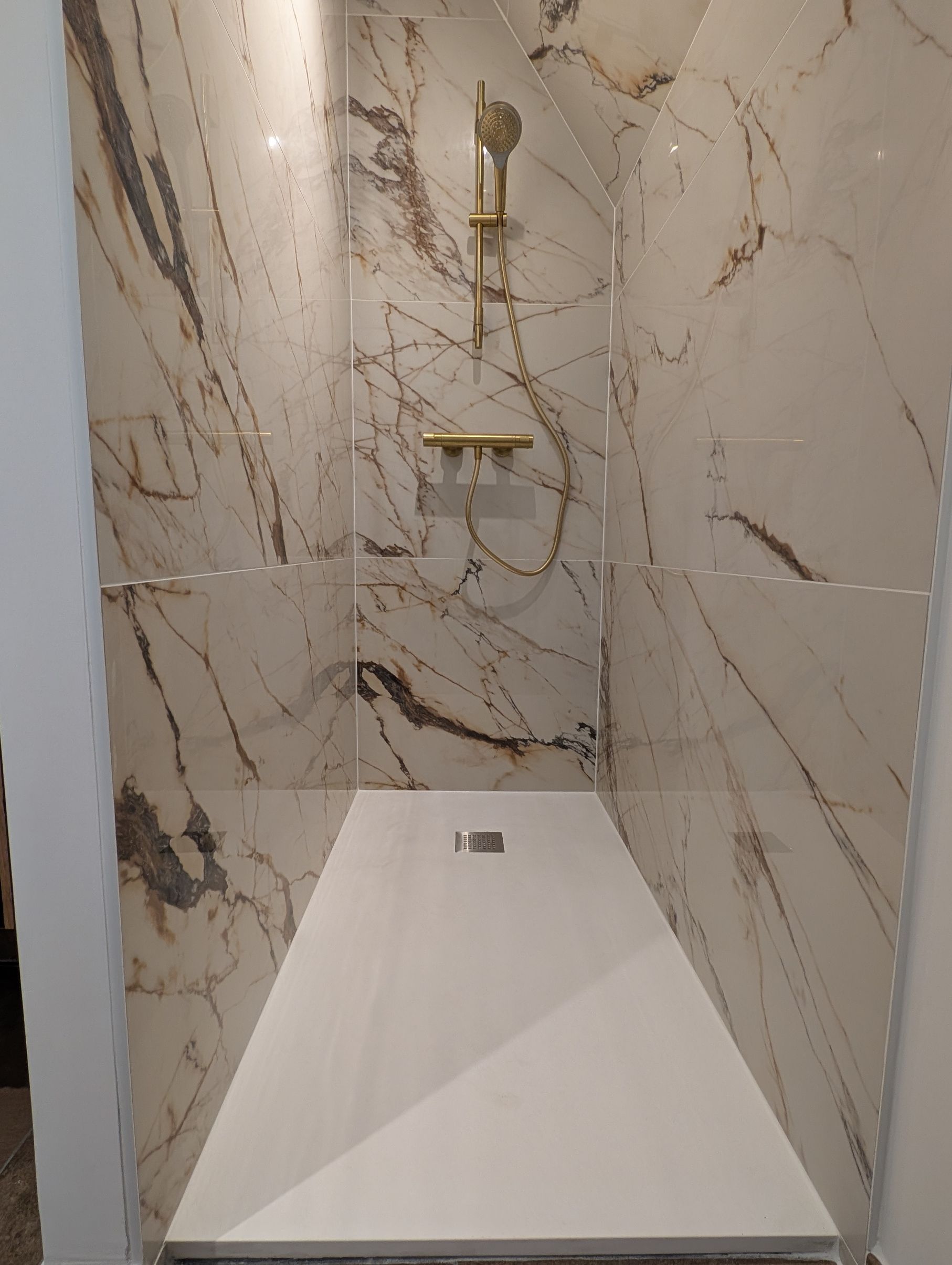Douche blanche avec robinetterie dorée et murs à motif de marbre.
