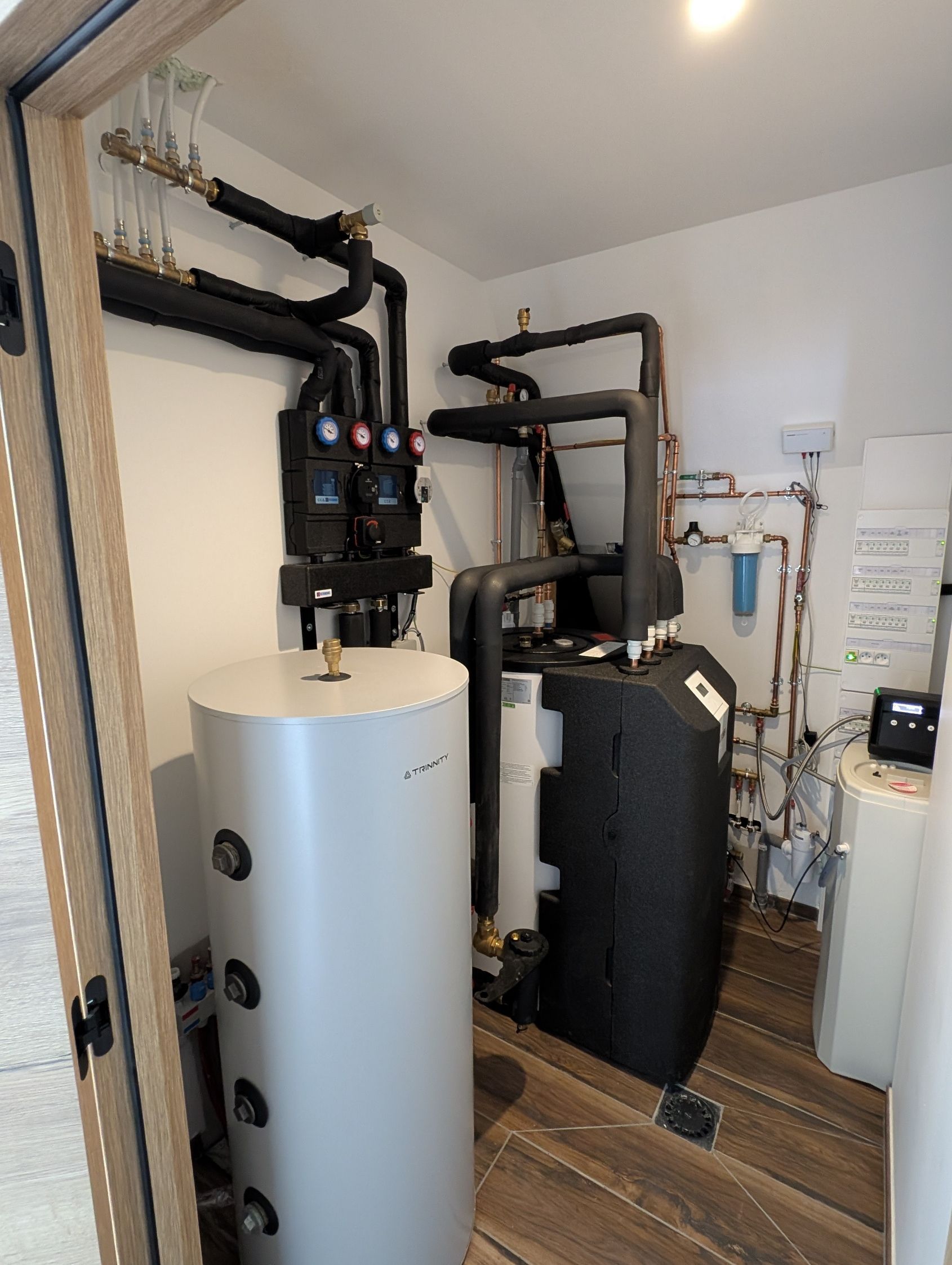 Une Chaufferie avec un Ballon Tampon, une pompe à chaleur et la plomberie associée contre un mur.