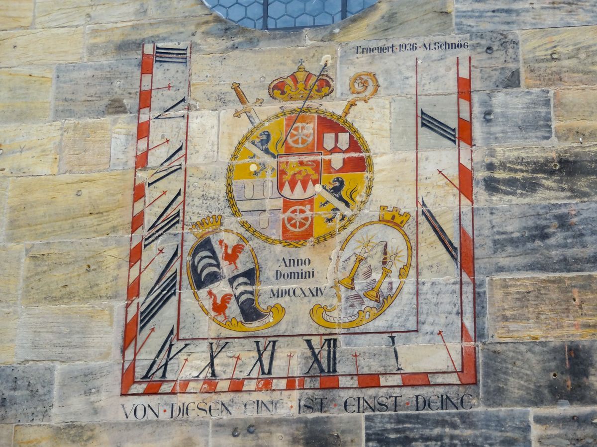 Sonnenuhr an der Außenfassade mit Wappen verziert und dem Hinweis auf die letzte Stunde