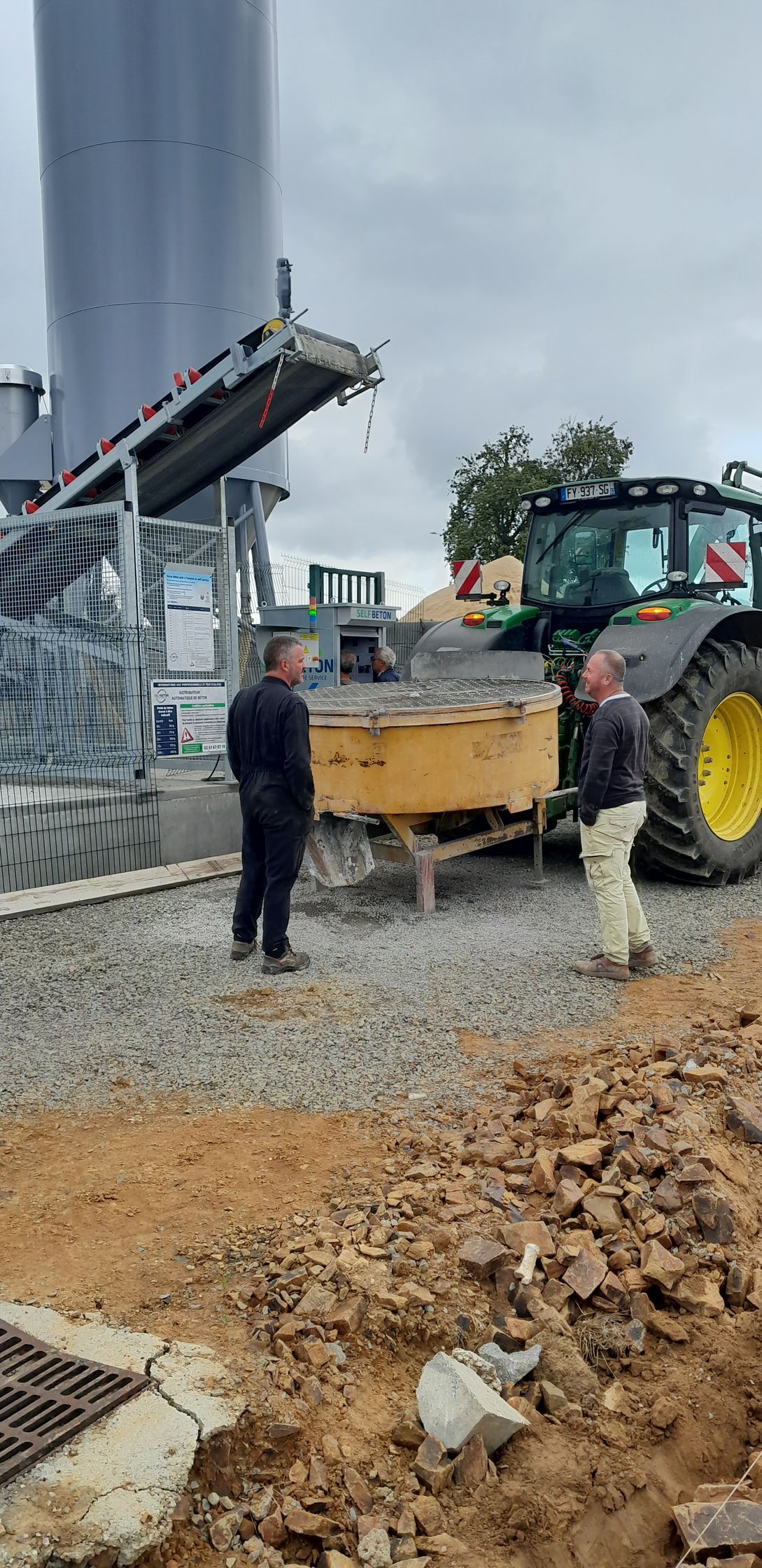 Deux personnes devant un conteneur de béton avec un tamis