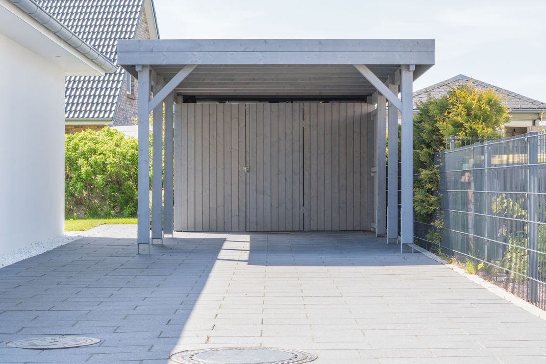 Allée couverte avec un abri pour voiture, à côté d’une maison et d’une terrasse pavée.