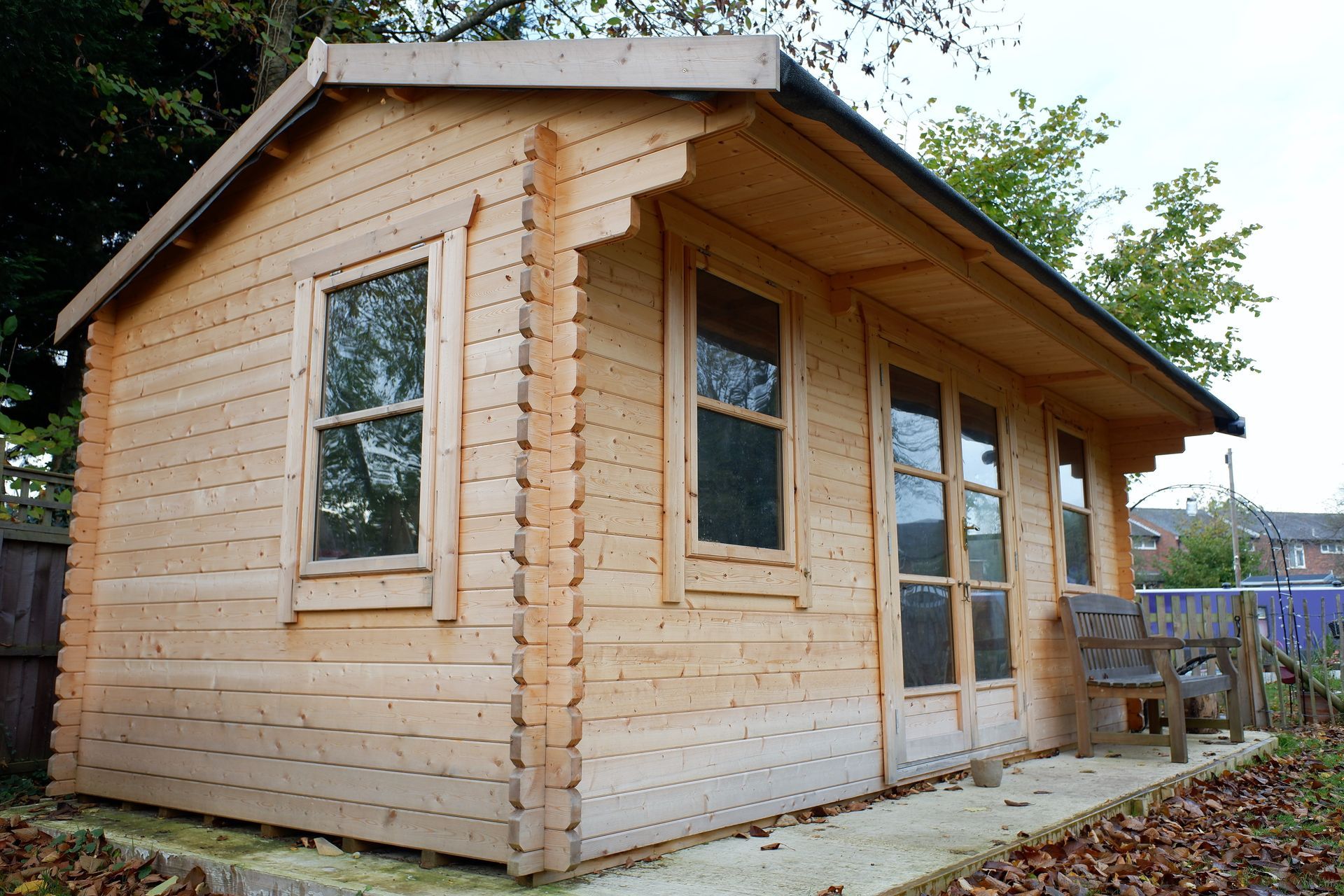 Cabane de jardin en bois avec deux fenêtres et une porte d’entrée, vue de trois quarts avant gauche dans un jardin.