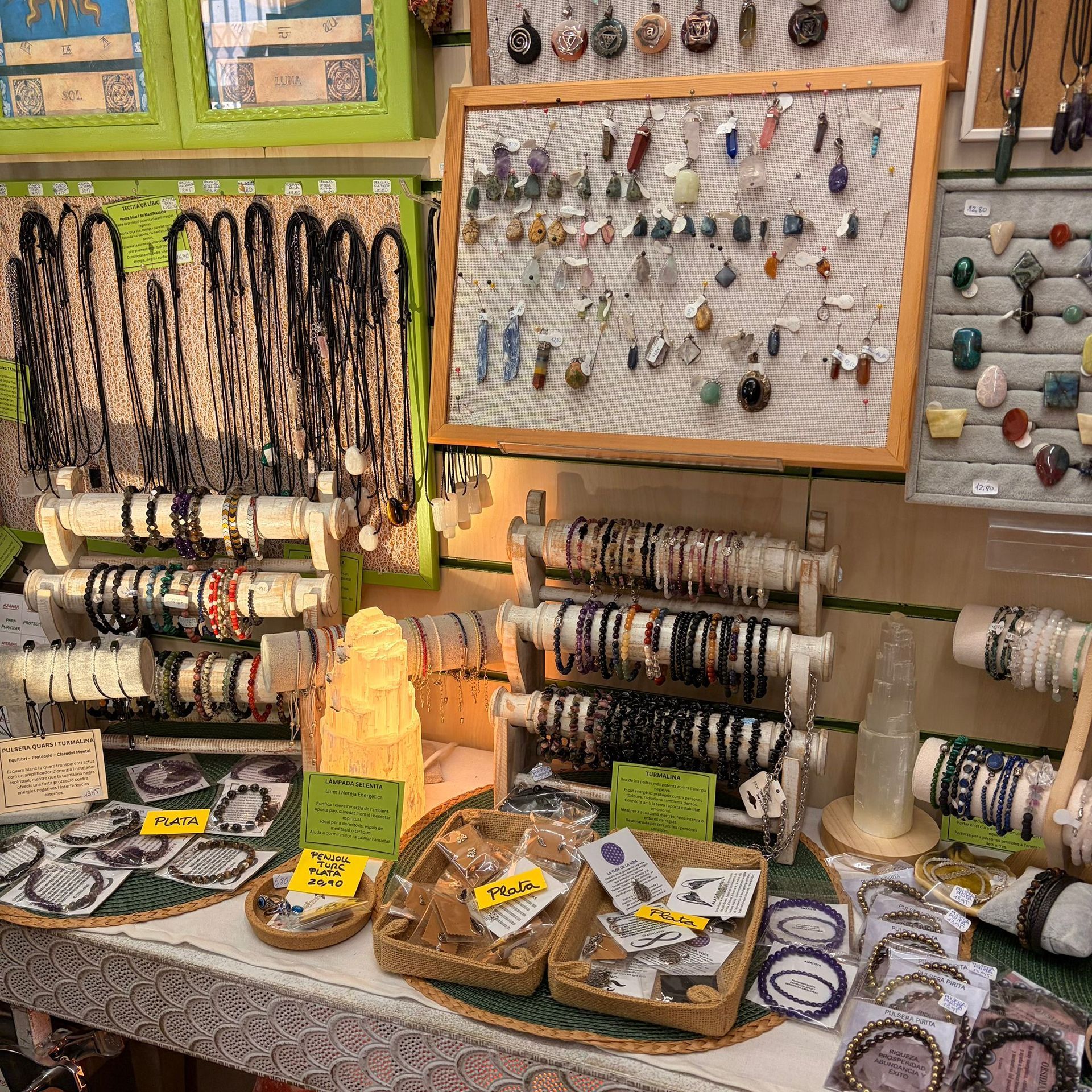 Exhibición de joyas: collares, pulseras y anillos en estantes, un tablero perforado y cestas, en una tienda.