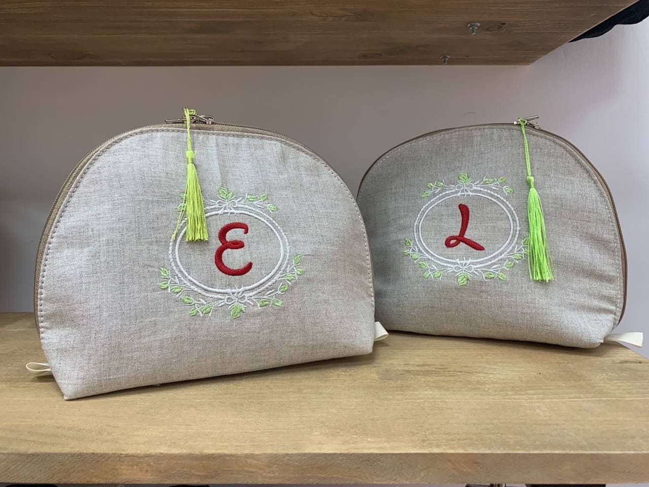 Dos bolsas de cosméticos con las letras e y l bordadas están sobre un estante de madera.