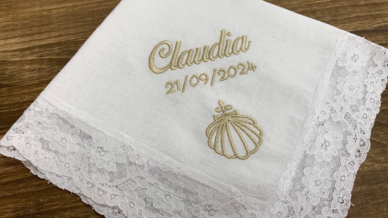 Un pañuelo blanco con el nombre Claudia bordado está sobre una mesa de madera.