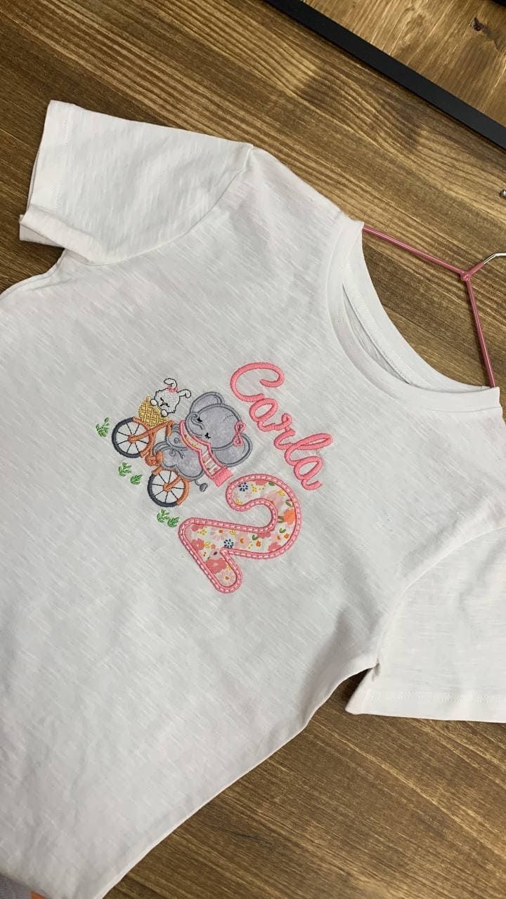 Una camiseta blanca con una bicicleta encima está colgada en una percha en un suelo de madera.