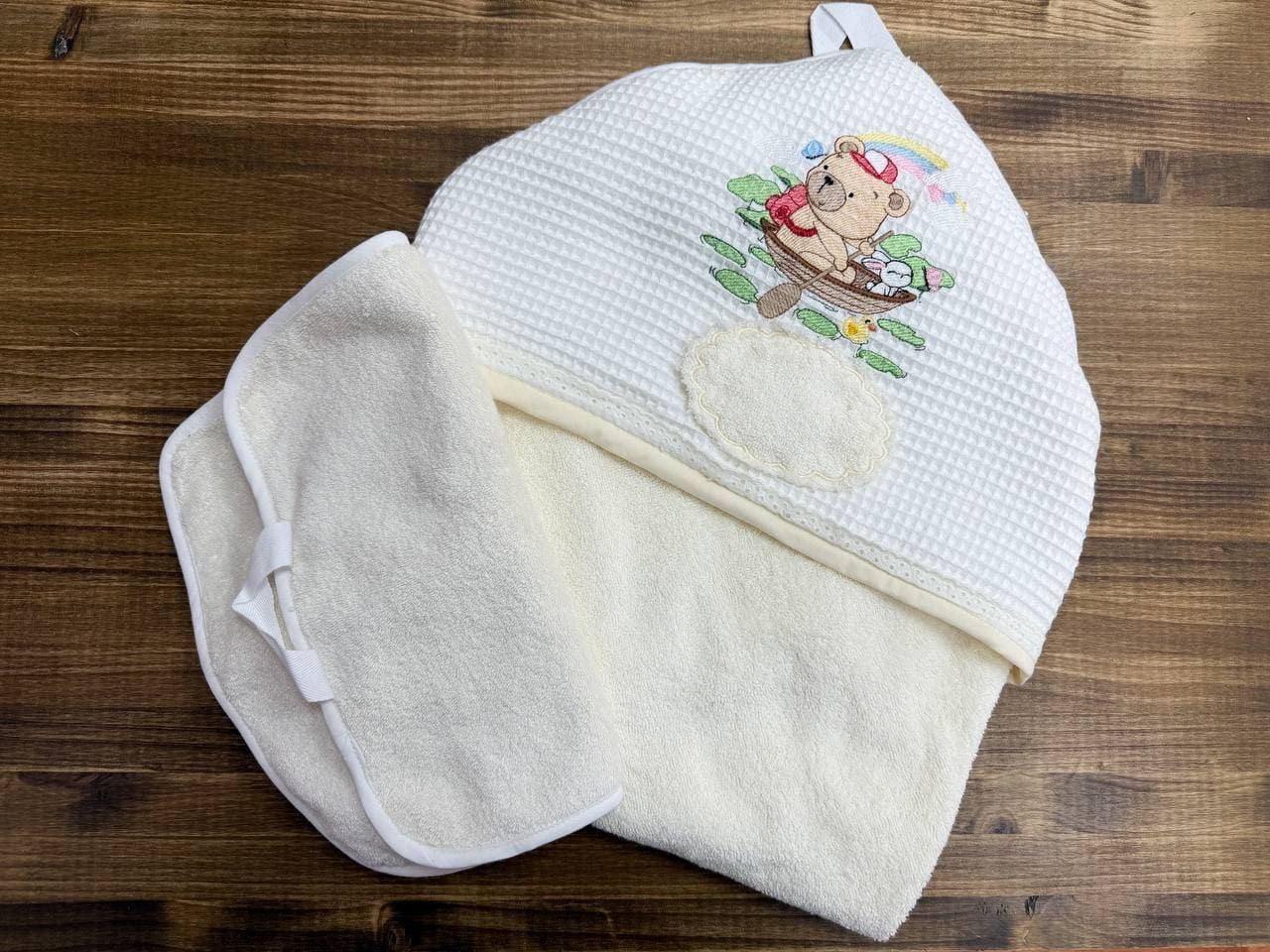 Una toalla blanca con un osito de peluche bordado está sobre una mesa de madera.