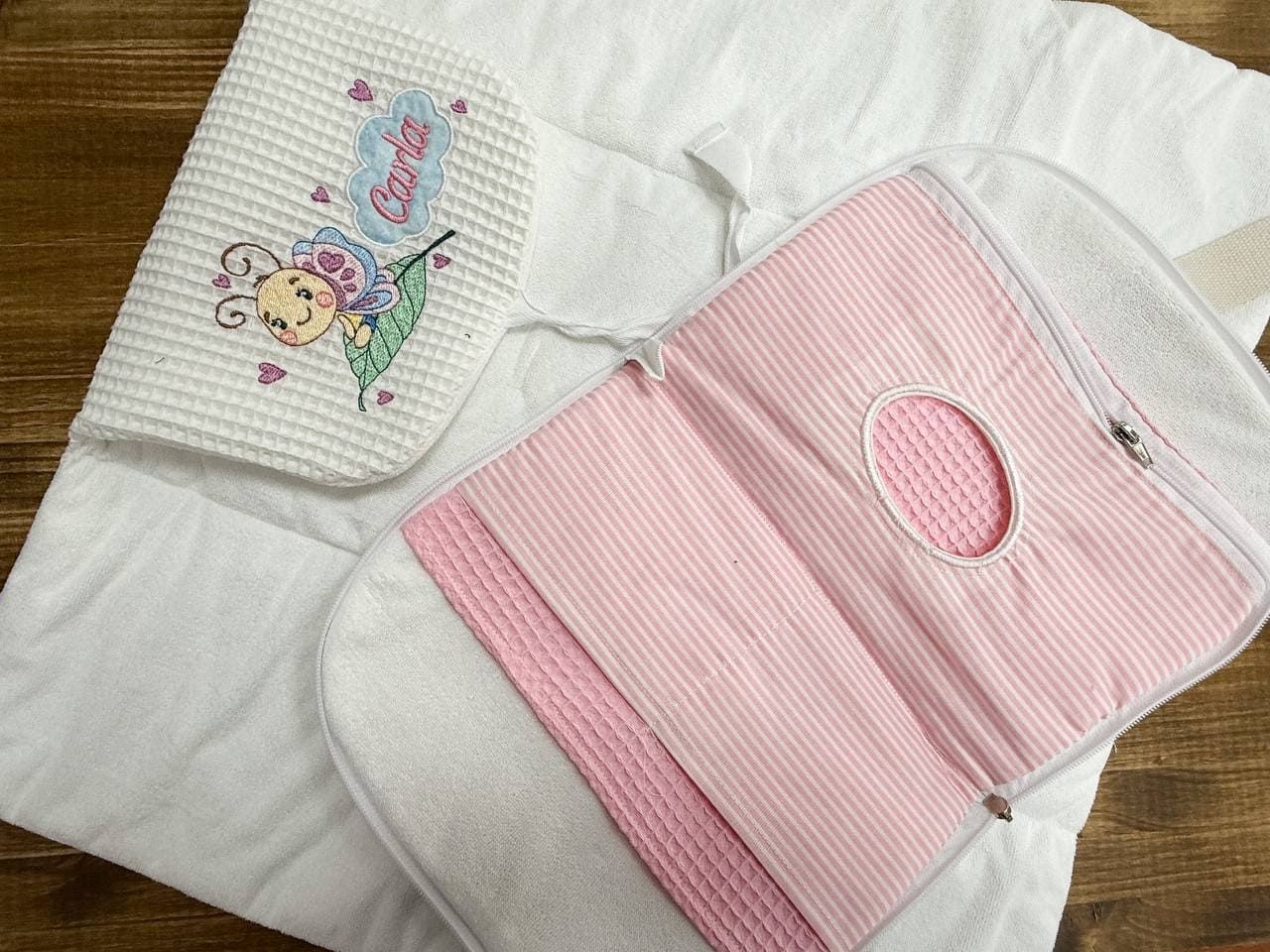 Una bolsa de pañales rosa está encima de una manta blanca sobre una mesa de madera.