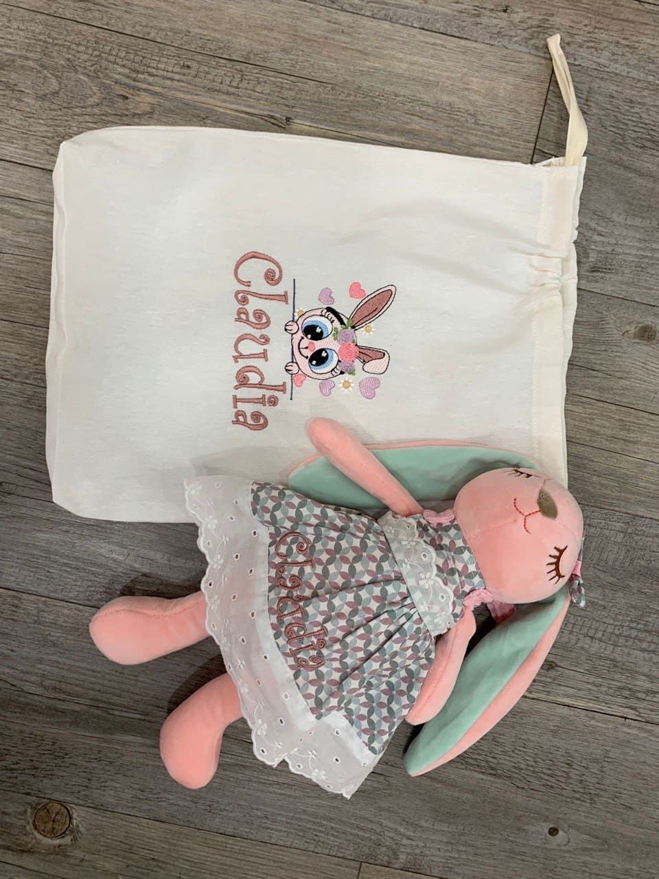 Un conejito de peluche está sentado junto a una bolsa que dice Claudia.