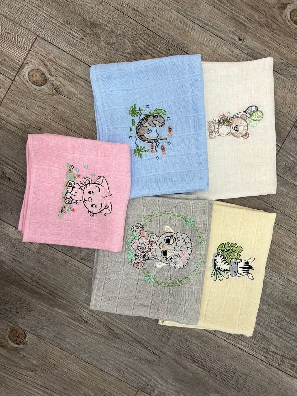 Un grupo de toallas con animales bordados en ellas están colocadas sobre un suelo de madera.