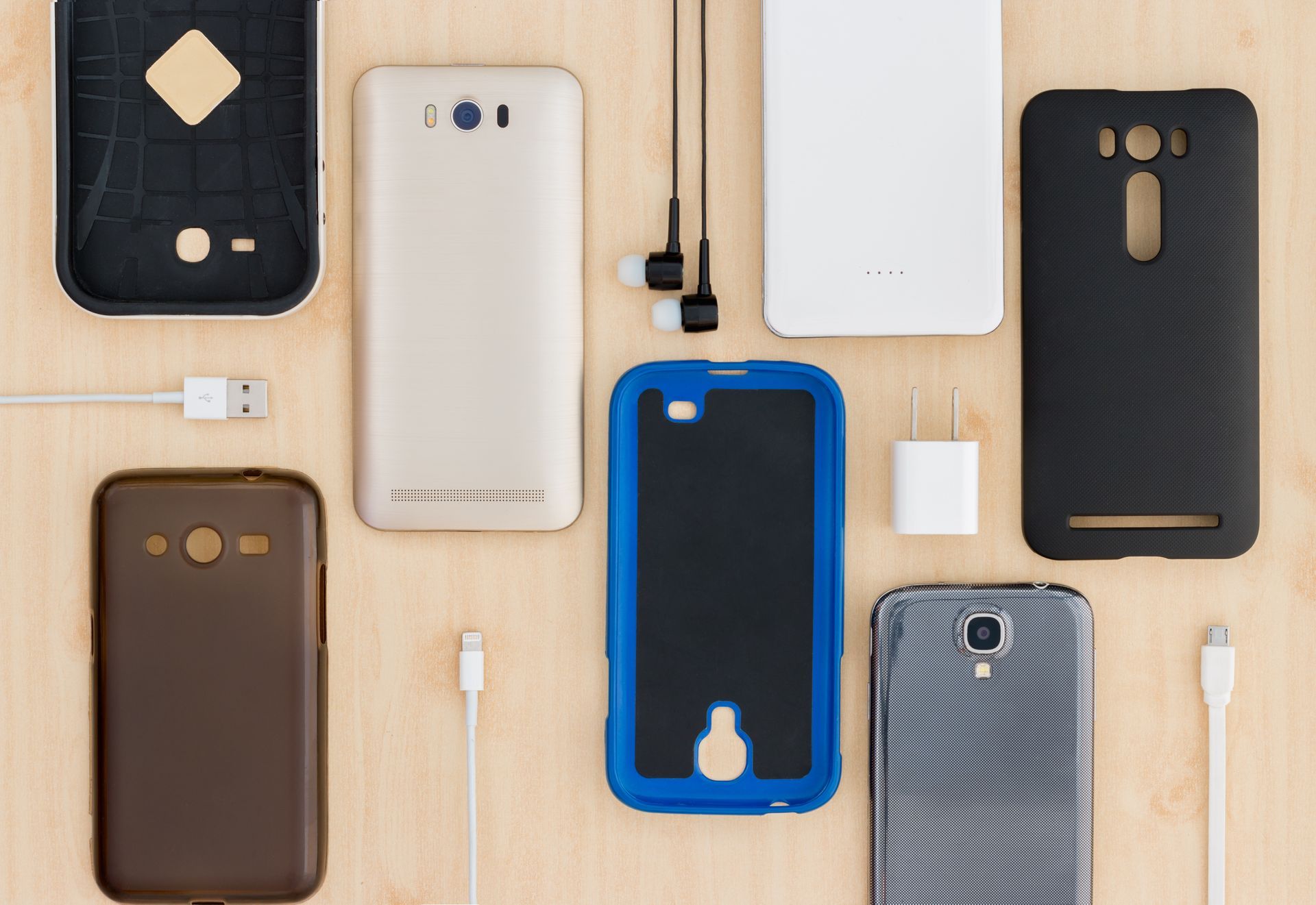 Divers étuis de Smartphones et câbles de chargement disposés sur une surface en bois clair.