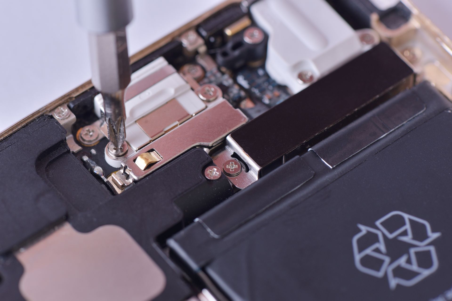 Un tournevis serre une vis à l'intérieur d'un Smartphone, près de la batterie et du circuit imprimé.