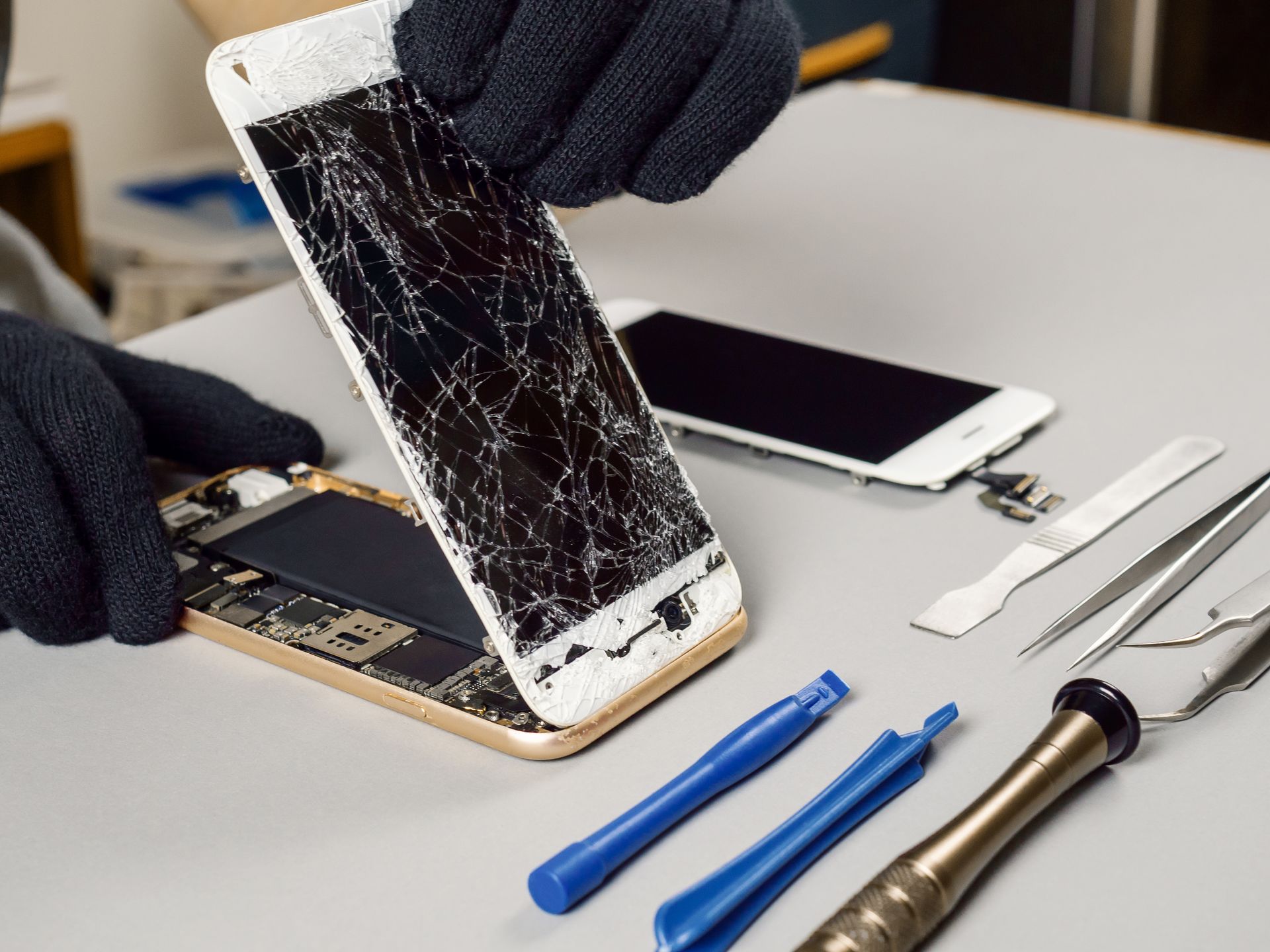 Des mains gantées réparent un Smartphone fissuré à l'aide d'outils sur un établi.