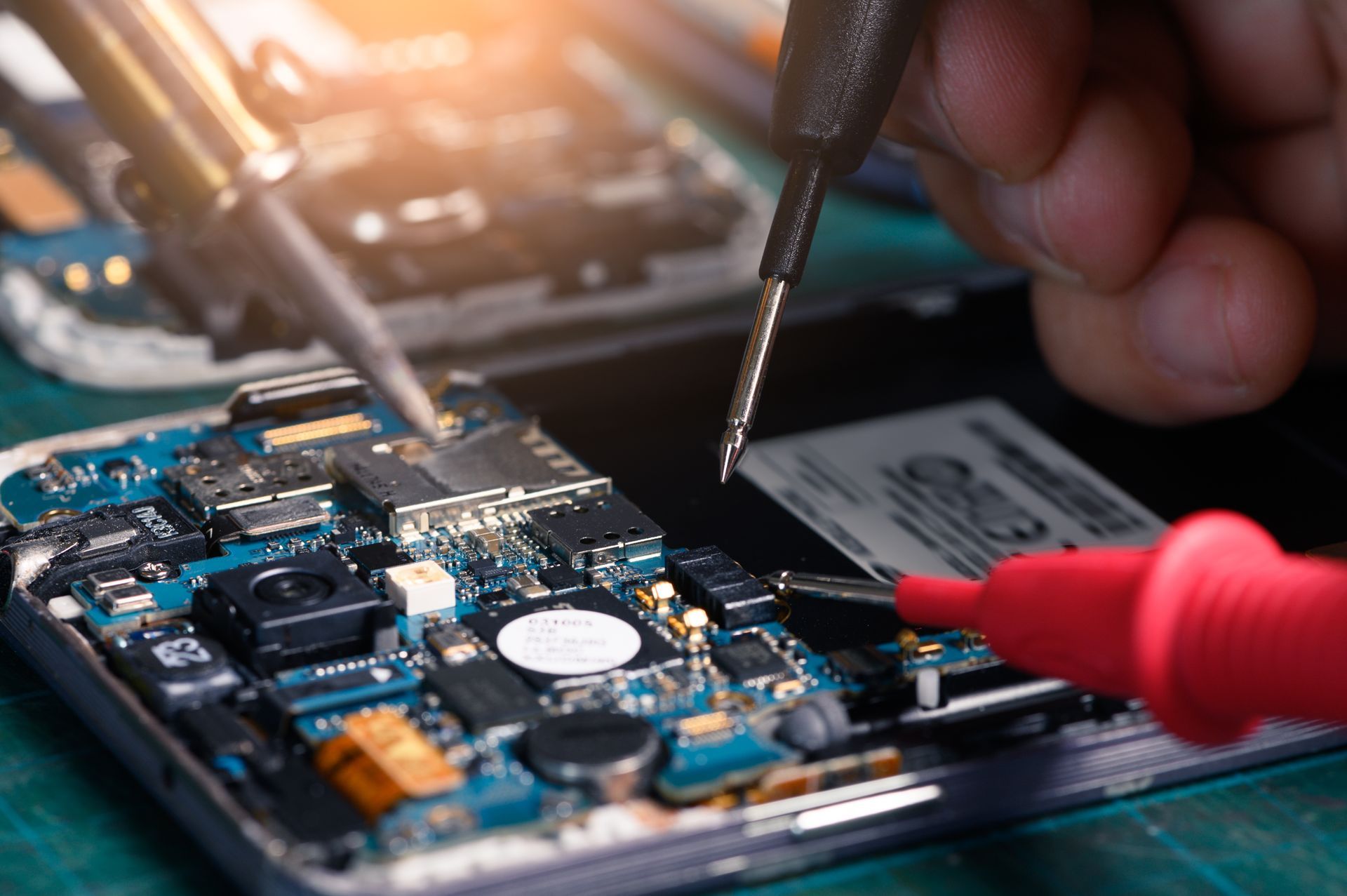 Un technicien examine la carte de circuit imprimé d'un Smartphone à l'aide de cordons de test et d'outils de précision.