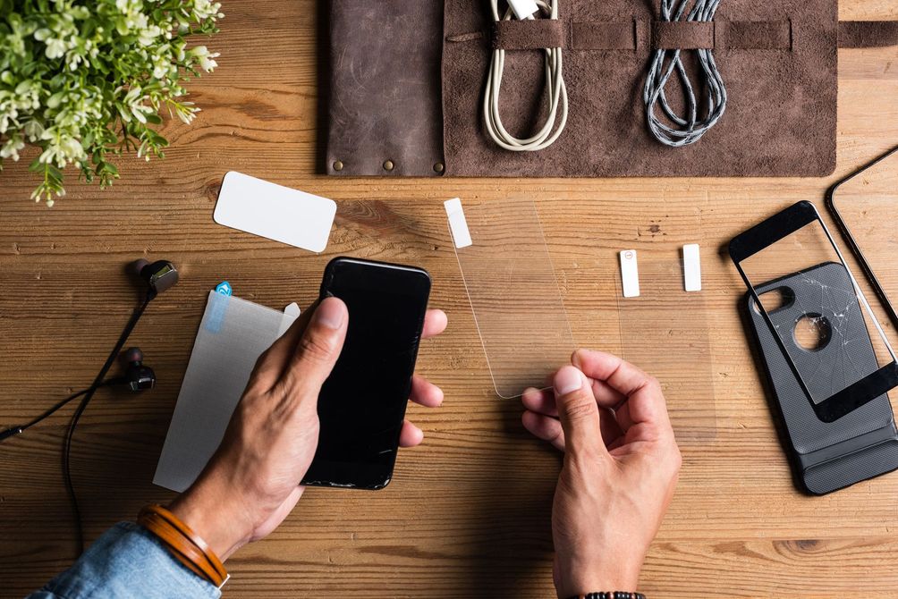 Des mains assemblent un Smartphone noir sur un établi en bois, avec des outils et des pièces à proximité.