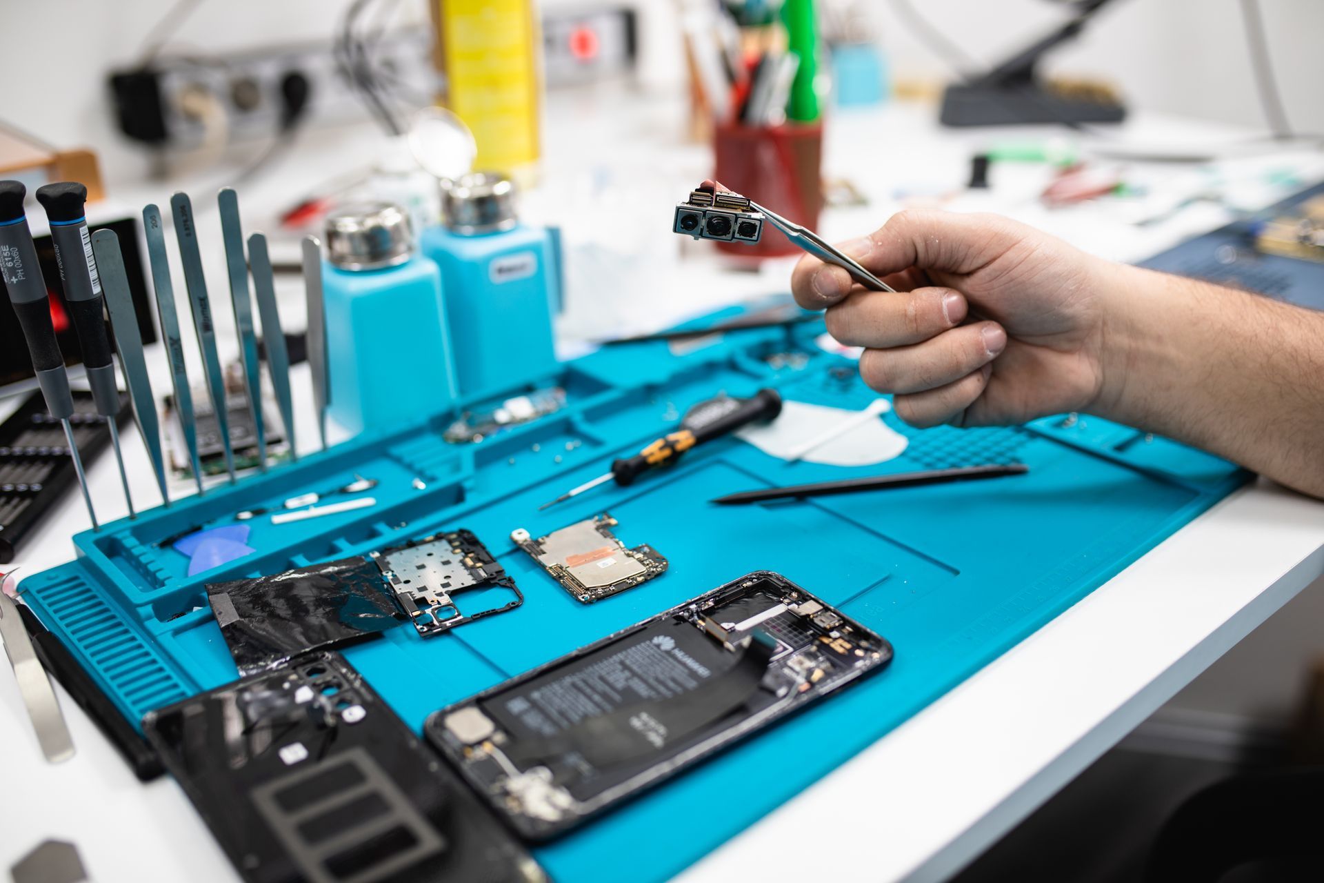 Un technicien répare un Smartphone sur un tapis de travail bleu, entouré d'outils et de pièces détachées de téléphone.