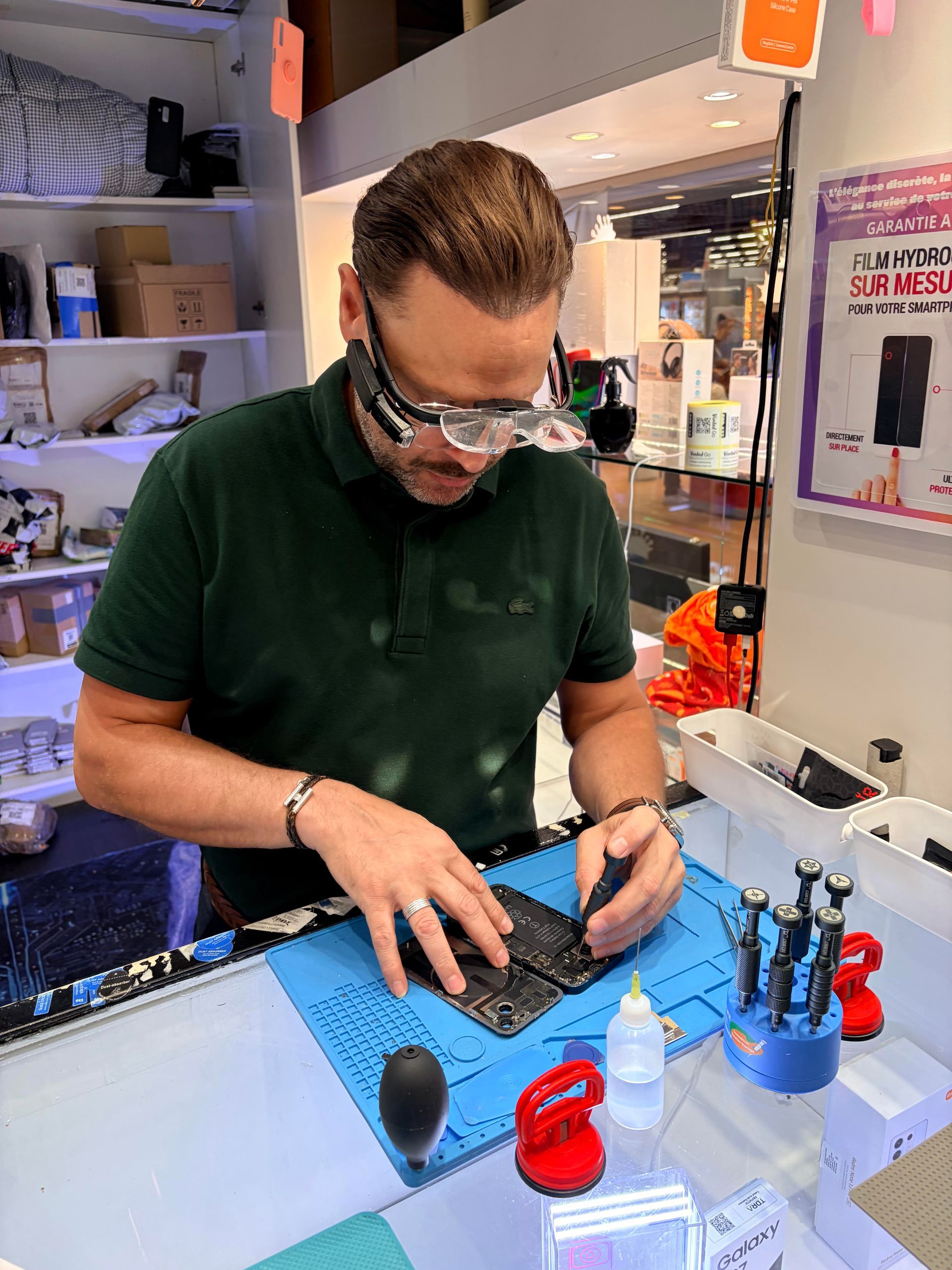 Une personne ajuste des lunettes dans un atelier de réparation d'optique, avec des outils et des pièces sur un tapis bleu.