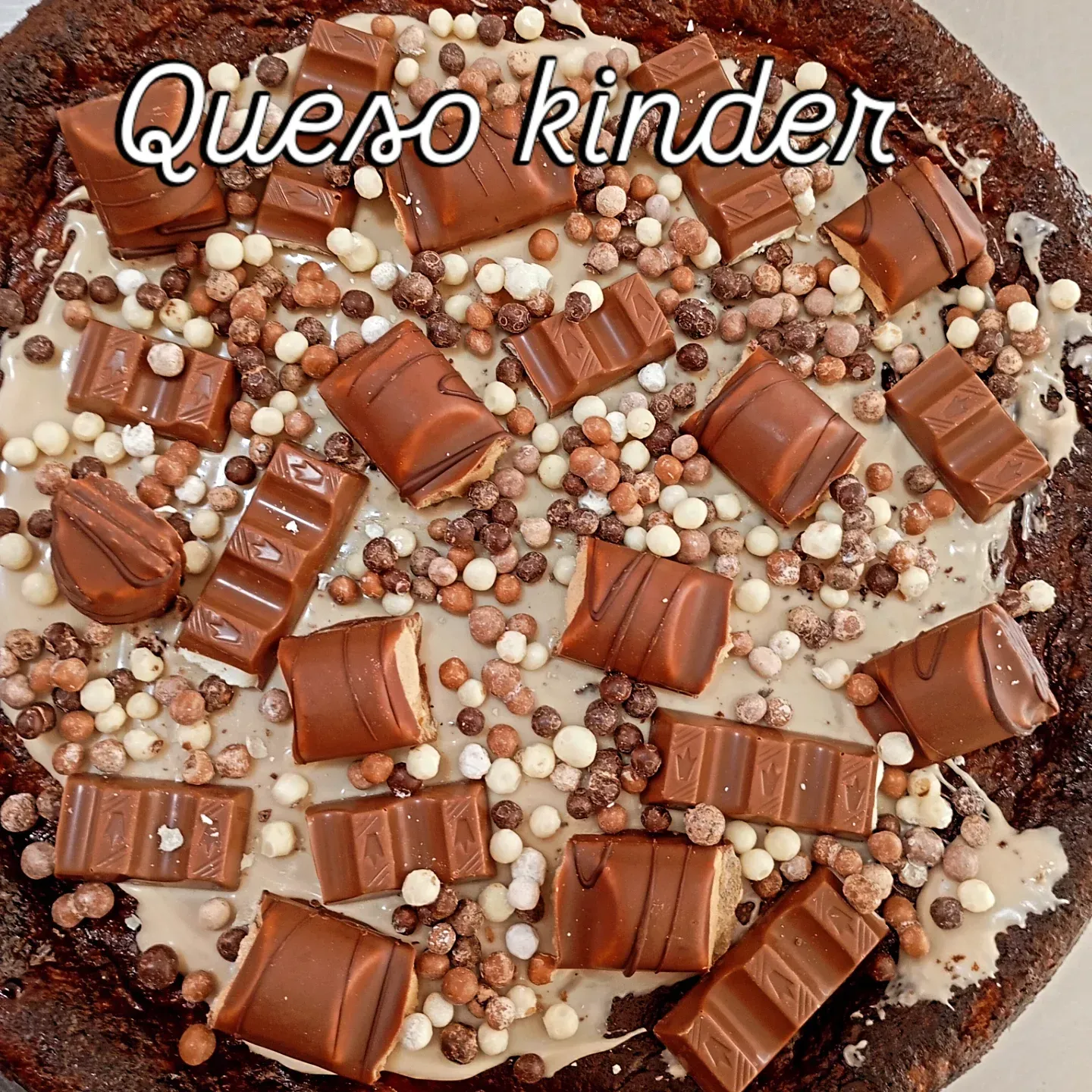 Postre cubierto de chocolate con la etiqueta “Queso Kinder”, barras Kinder y chispas de perlas.