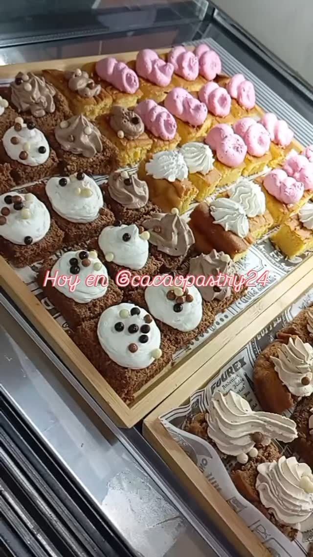 Bandeja de cupcakes surtidos decorados con glaseado rosa y marrón en una vitrina de pastelería.