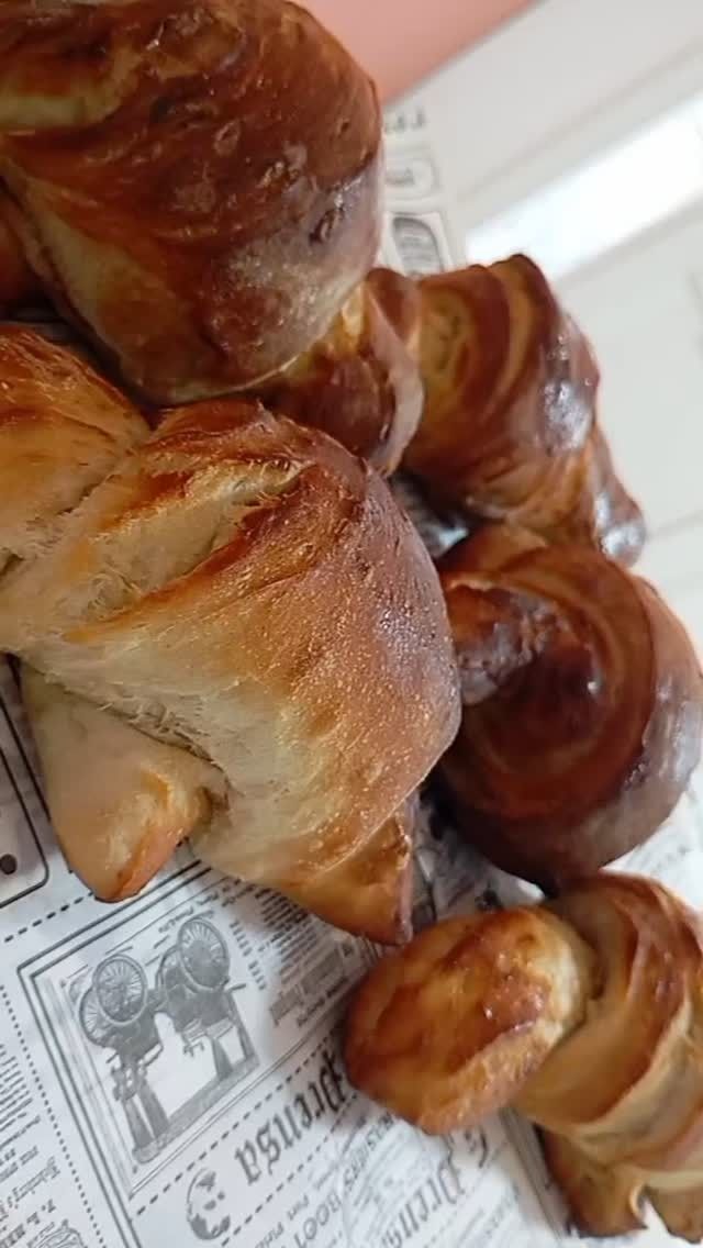 Croissants y pasteles dorados apilados en una bandeja forrada con papel de periódico.
