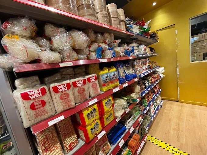 Estantes llenos de productos alimenticios asiáticos en una tienda, incluidos fideos, arroz y productos envasados.