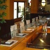 Restaurante con separadores transparentes en un mostrador de madera, cubiertos y una parrilla en el frente.