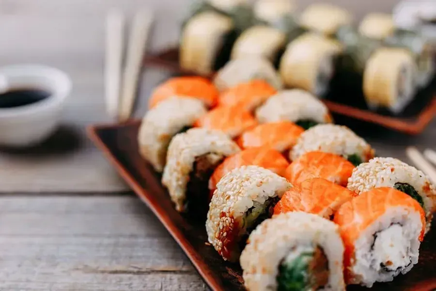 Plato de sushi con rollos, nigiri de salmón, salsa de soja y palillos sobre una mesa de madera.