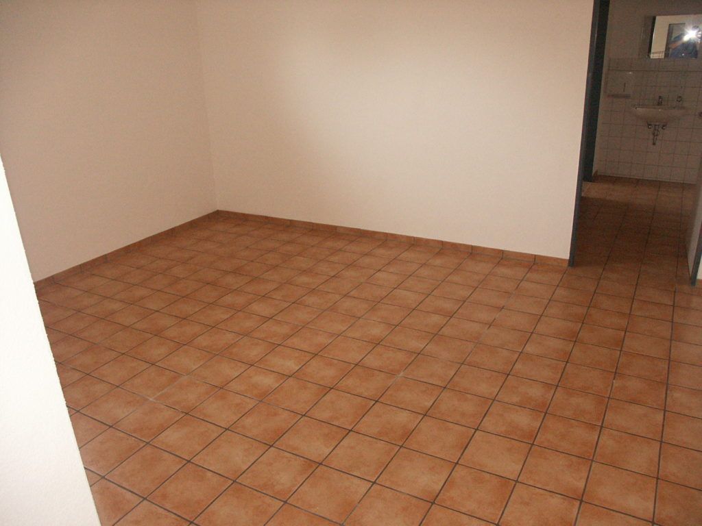 Leerer, gefliester Raum mit beigen Wänden und einer Tür zu einem Badezimmer auf der rechten Seite.